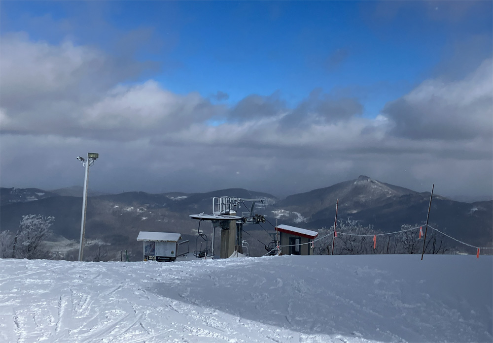Skiers on a snowy slope at a North Carolina ski resort with forested hills